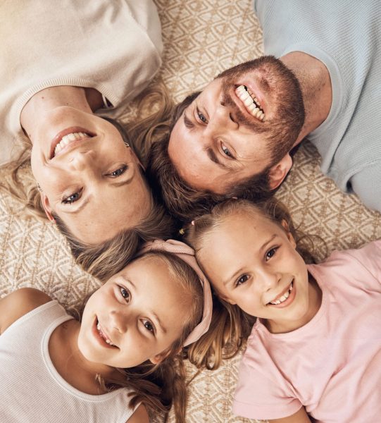Love, portrait and top view of happy family on a floor bonding, relax and having fun at home together. Face, smile and children with parents lying in a living room with care, support or security.