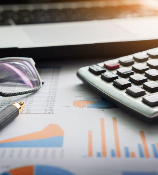 financial charts on the table with laptop, calculator, pen and glasses business concept.