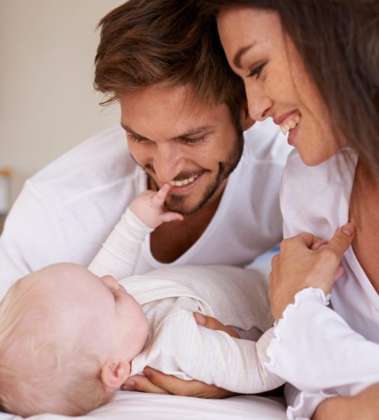 Happy father, mother and baby on bed for love, care and quality time together. Parents, newborn kid and relax in bedroom of family home with smile, childhood development and caring support of bonding.