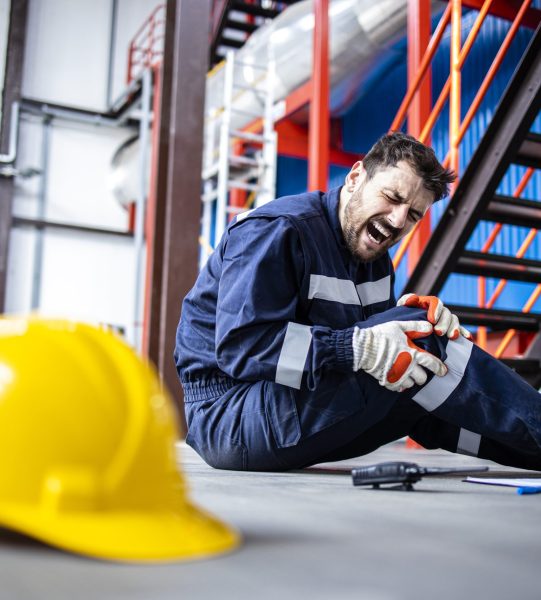 Injured factory worker having knee pain due to the fall from the steps. Safety at work concept.