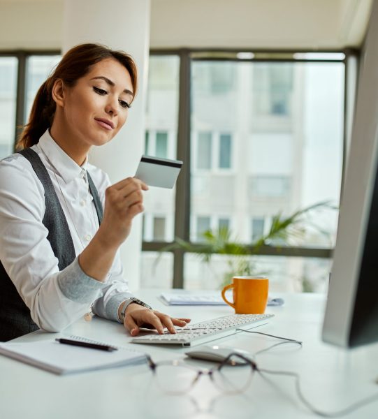 Smiling businesswoman using credit card and computer while buying on the internet in the office.