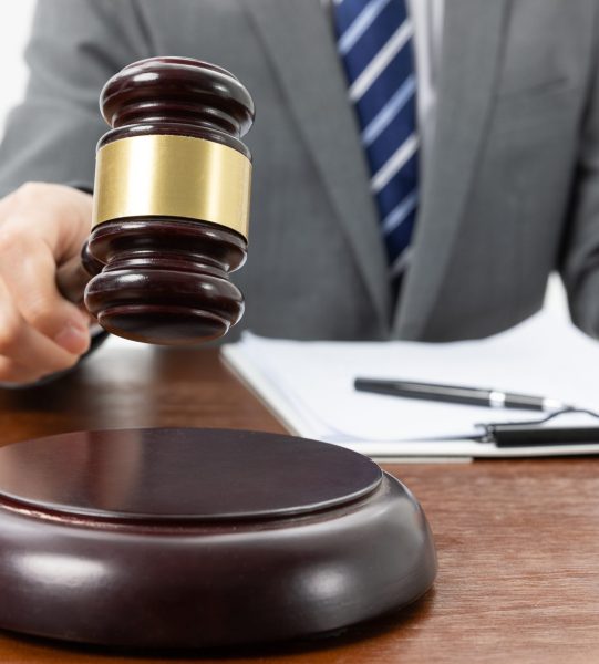 A closeup shot of a person with a gavel in hand and papers on the table